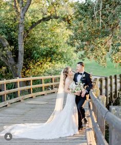 a bride and groom standing on a bridge in front of the trees at their wedding