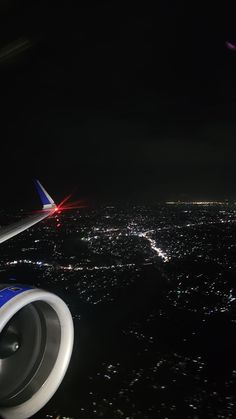 an airplane wing at night with the lights on and city lights in the sky behind it