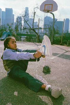 a young person sitting on the ground with a basketball in their hand and buildings in the background