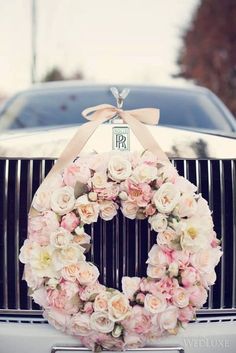 a wreath on the front of a car is adorned with pink and white flowers, tied with a ribbon