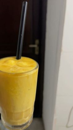 a tall glass filled with yellow liquid and a black straw sticking out of the top