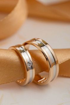 two gold wedding rings sitting on top of each other with a diamond in the middle