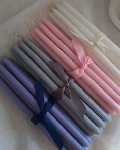 several different colored candles with ribbons tied around them on a white tablecloth, one is blue and the other is pink