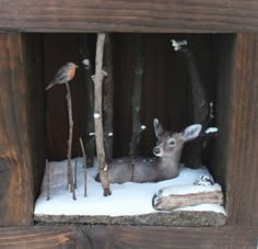 a fake deer in a wooden box with snow on the ground and birds perched on branches