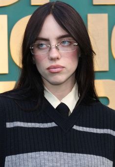 a woman wearing glasses standing in front of a green and gold wall with letters on it