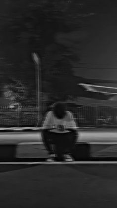 a man sitting on a bench in front of a street sign at night with his feet crossed