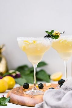 two glasses filled with lemonade and blackberries on a cutting board next to some leaves