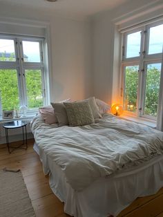 a white bed sitting in a bedroom next to two large windows on top of a wooden floor