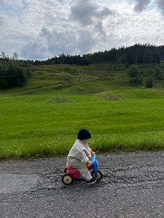 a little boy riding a toy bike down a road next to a lush green field