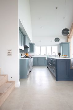 a kitchen with blue cabinets and stairs leading up to the upper floor, in front of a large window