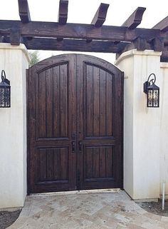 a large wooden door in front of a white building with two lanterns on it's side