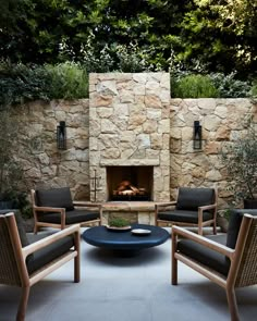 an outdoor fireplace with chairs and a table in front of it, surrounded by greenery