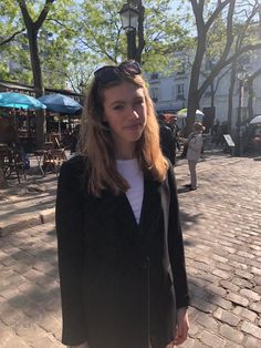 a woman standing on a brick road in front of trees and buildings with her hand under her ear