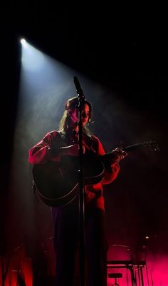 a man holding a guitar while standing in front of a microphone on top of a stage