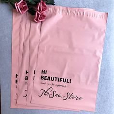 three pink shopping bags sitting on top of a table with flowers in the bag next to them