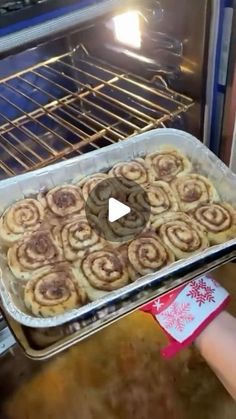 a person holding a pan full of cinnamon rolls in front of an oven with the door open