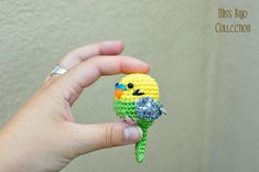 a hand holding a small crocheted bird with a flower in it's beak