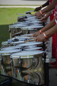 several people are lined up with drums on the side of the road and one person is wearing an orange wristband