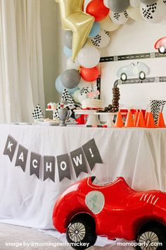 a red toy car sitting in front of a table with balloons and streamers on it