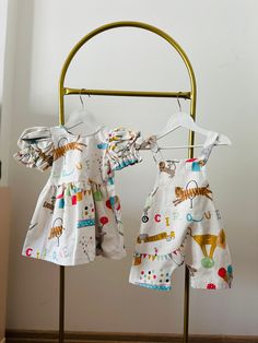 two baby clothes are hanging on a metal rack in front of a white wall and wooden floor