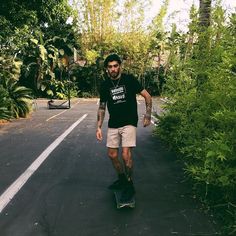 a man riding a skateboard down the middle of a road next to tall trees