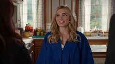 a woman standing in a kitchen talking to another woman who is wearing a blue jacket