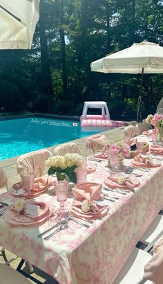 an outdoor table set up with pink and white plates, napkins and flowers near a swimming pool