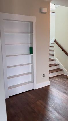 an empty living room with white bookcases and wood flooring in front of the stairs