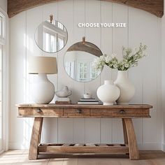 a wooden table topped with white vases next to a mirror