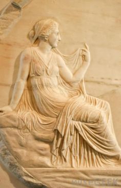 a statue of a woman sitting on top of a stone slab in front of a wall