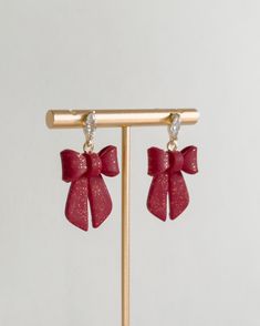 a pair of red bow earrings hanging from a wooden stick