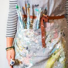 a woman is wearing an apron with paintbrushes in it and she has her hands behind her back