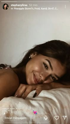 a woman laying on top of a bed next to a white wall and smiling at the camera