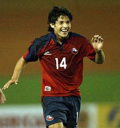 a soccer player is running with the ball in his hand and smiling for the camera