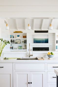 a kitchen with white cabinets and open shelving above the sink is filled with fruit