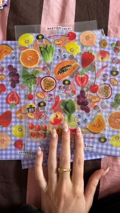 a woman's hand is holding up two cards with fruit and vegetables on them