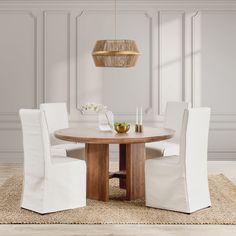 a dining room table with white chairs and a rug on the floor in front of it