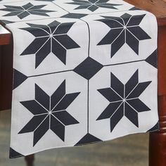 black and white quilted table runner with four stars on it, sitting on top of a wooden table