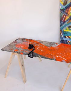 an orange and grey table with a black object on it's legs in front of a painting