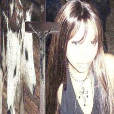 a girl with long hair wearing a black tank top standing in front of a cross