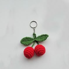 two crocheted cherries hanging from a keychain on a white surface