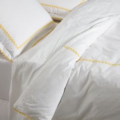 a bed with white sheets and yellow trimmings on the pillowcase is shown