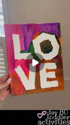 someone holding up a piece of art with the word love painted on it in front of them