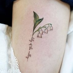 a small lily of the valley tattoo on the right side of the thigh with words written below it