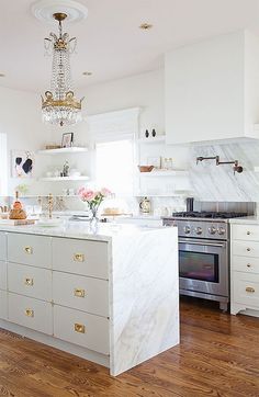 a white kitchen with marble counter tops and gold pulls on the cabinet doors is pictured in this image