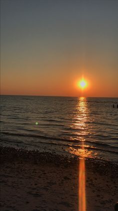 the sun is setting over the water on the beach