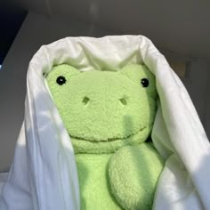 a green frog stuffed animal wrapped up in a white blanket with its eyes wide open