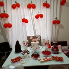 a table topped with a cake and lots of desserts next to a window covered in red balloons