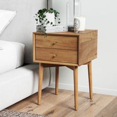 a bedside table with two drawers and a plant on top, next to a bed