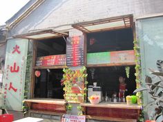 an outside view of a restaurant with signs on the wall and plants growing out of the windows